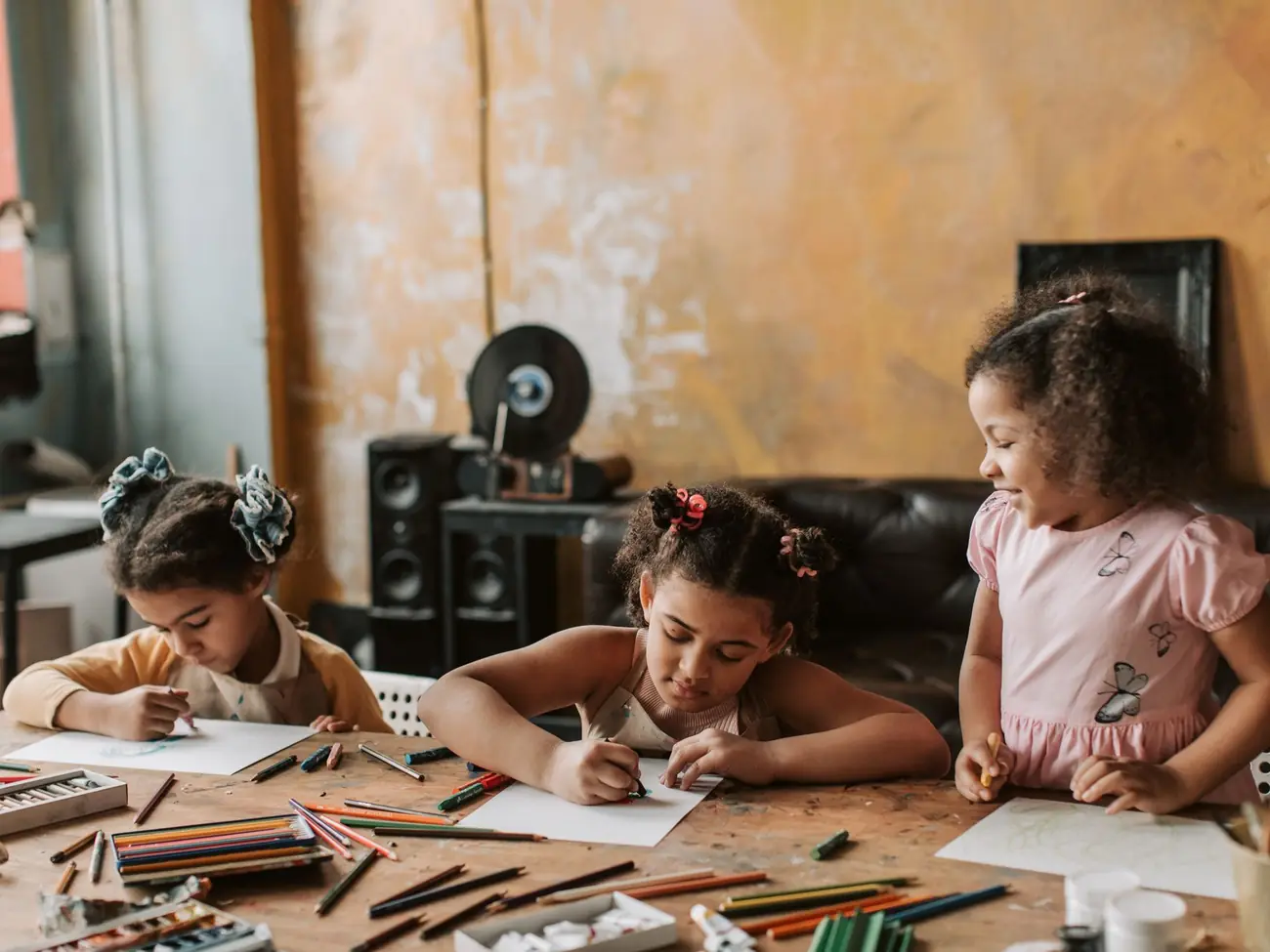 Three girls drawing together at a table full of art supplies